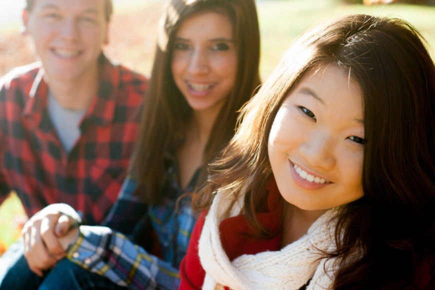 A diverse group of high school friends smiling on the front of the school lawn